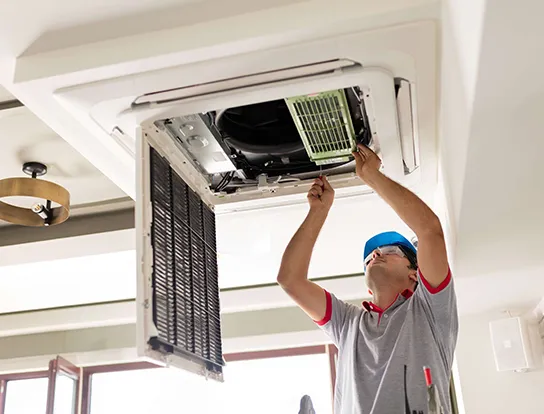 HVAC technician repairing a ceiling-mounted air conditioning unit with a screwdriver.